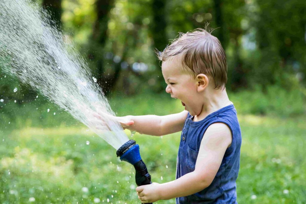 Kind spielt im Juni mit Wasser auf dem Rasen
