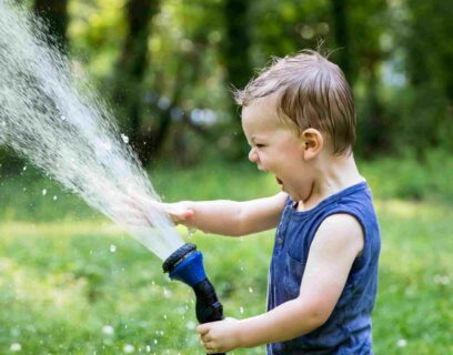 Kind spielt im Sommer mit Wasser auf dem Rasen