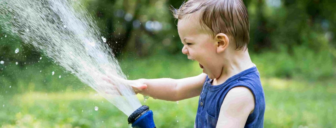 Kind spielt im Sommer mit Wasser auf dem Rasen