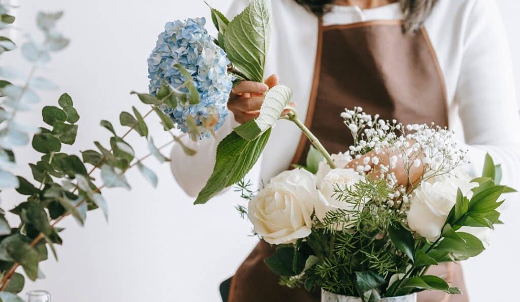 Hellblaue Hortensien werden in eine Vase mit weißen Rosen und Trockenblumen gesteckt.