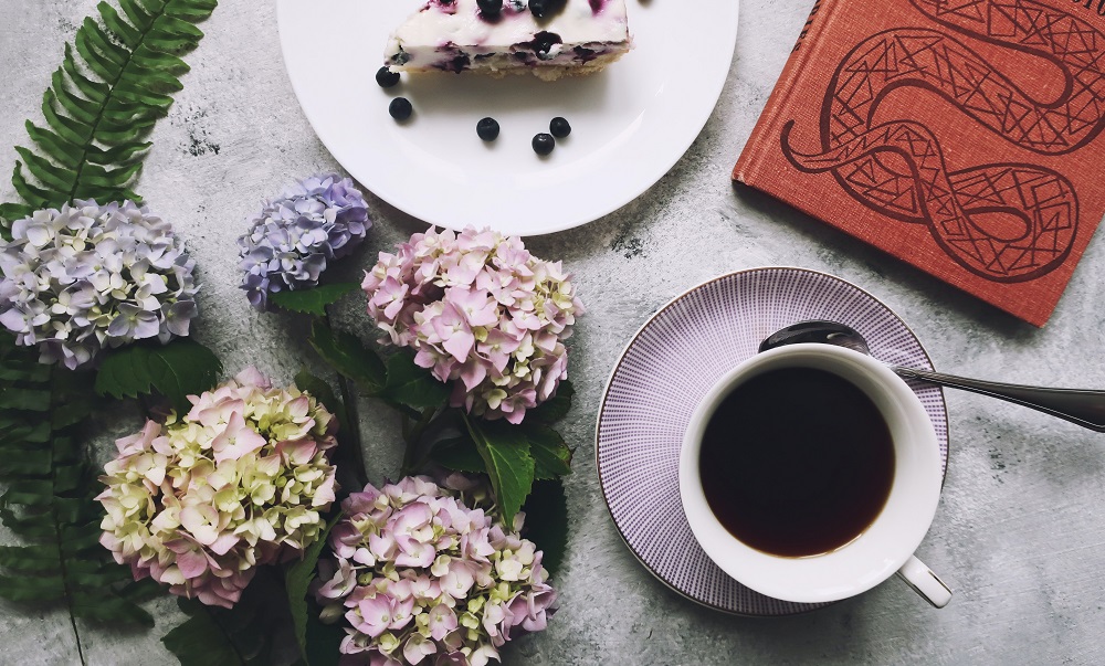 Ein schön gedeckter Kaffeetisch mit Kuchen, Kaffee, einem Buch und Hortensien.